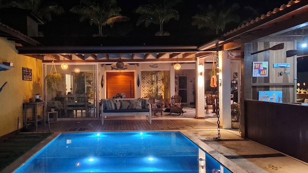 A pool area with a wooden deck, a seating area with a sofa and chairs, and a bar area with a sign that reads "POP ART". - Casa Santa María Búzios (Búzios)