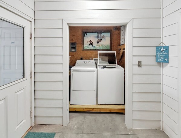 Un cuarto de lavandería con dos electrodomésticos blancos, un revestimiento de madera y un cuadro.