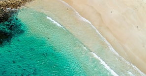 Vista aérea de una playa con aguas turquesas cristalinas y una orilla arenosa.