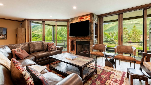 A living room with a fireplace, leather furniture, and large windows offering a view of the outdoors.