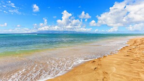 A beach with clear blue water, a sandy shore, and a distant mountain.