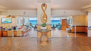 A lobby with a reception desk, a decorative infinity sculpture, a potted plant, and a view of the ocean.