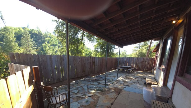 A covered patio area with stone flooring, wooden furniture, and a wooden fence.