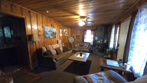 A cozy cabin interior with wooden walls, a leather sofa, a dining table, and a fireplace.