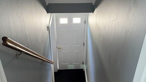 A staircase with wooden steps and a handrail, leading to a white door with two windows. - Peaceful 2-bedroom apartment with AC in Spring Lake Heights close to the beach. (Spring Lake)