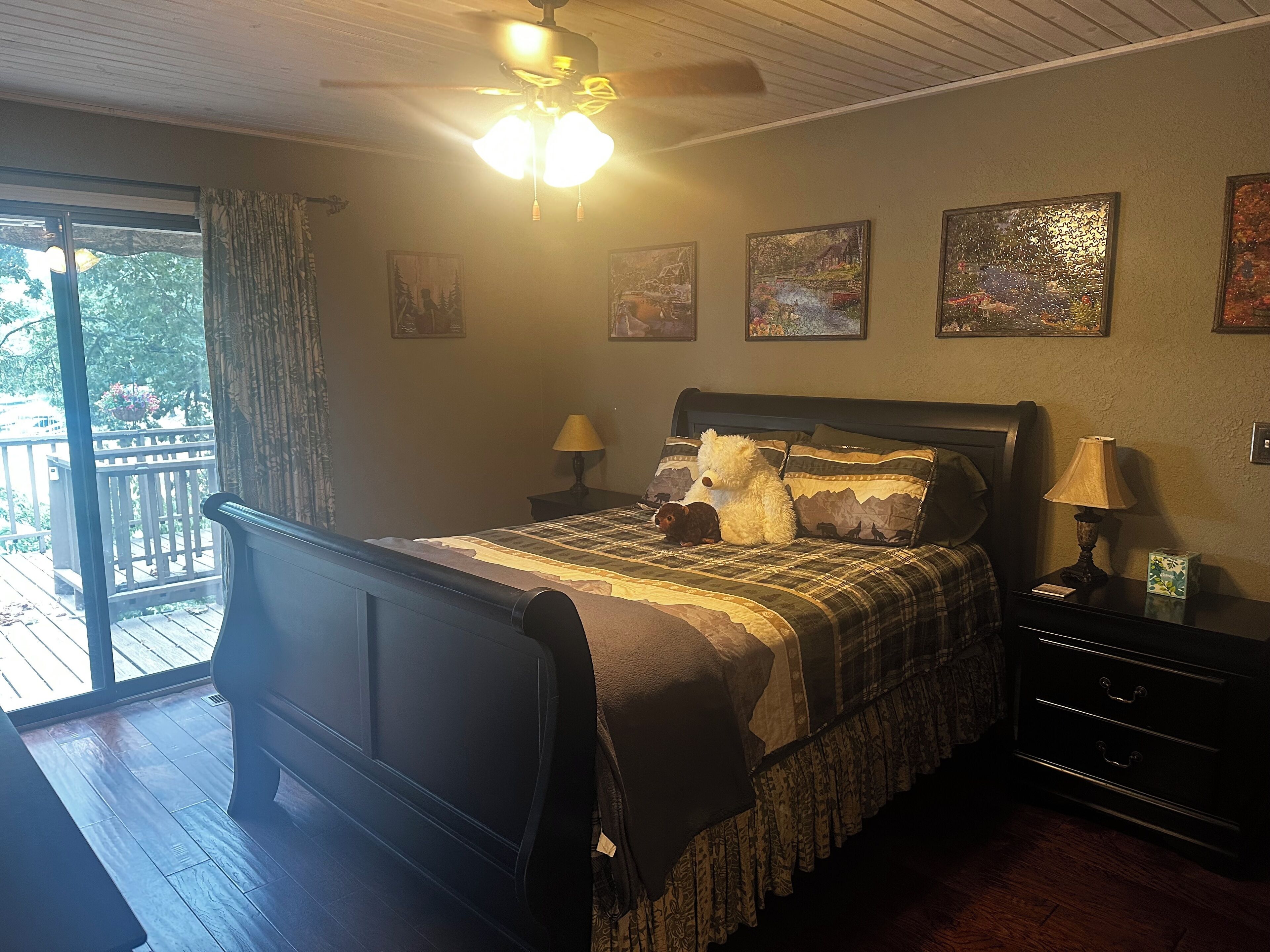 A bedroom with a bed, two bedside tables, a ceiling fan, and a view of the outdoors.