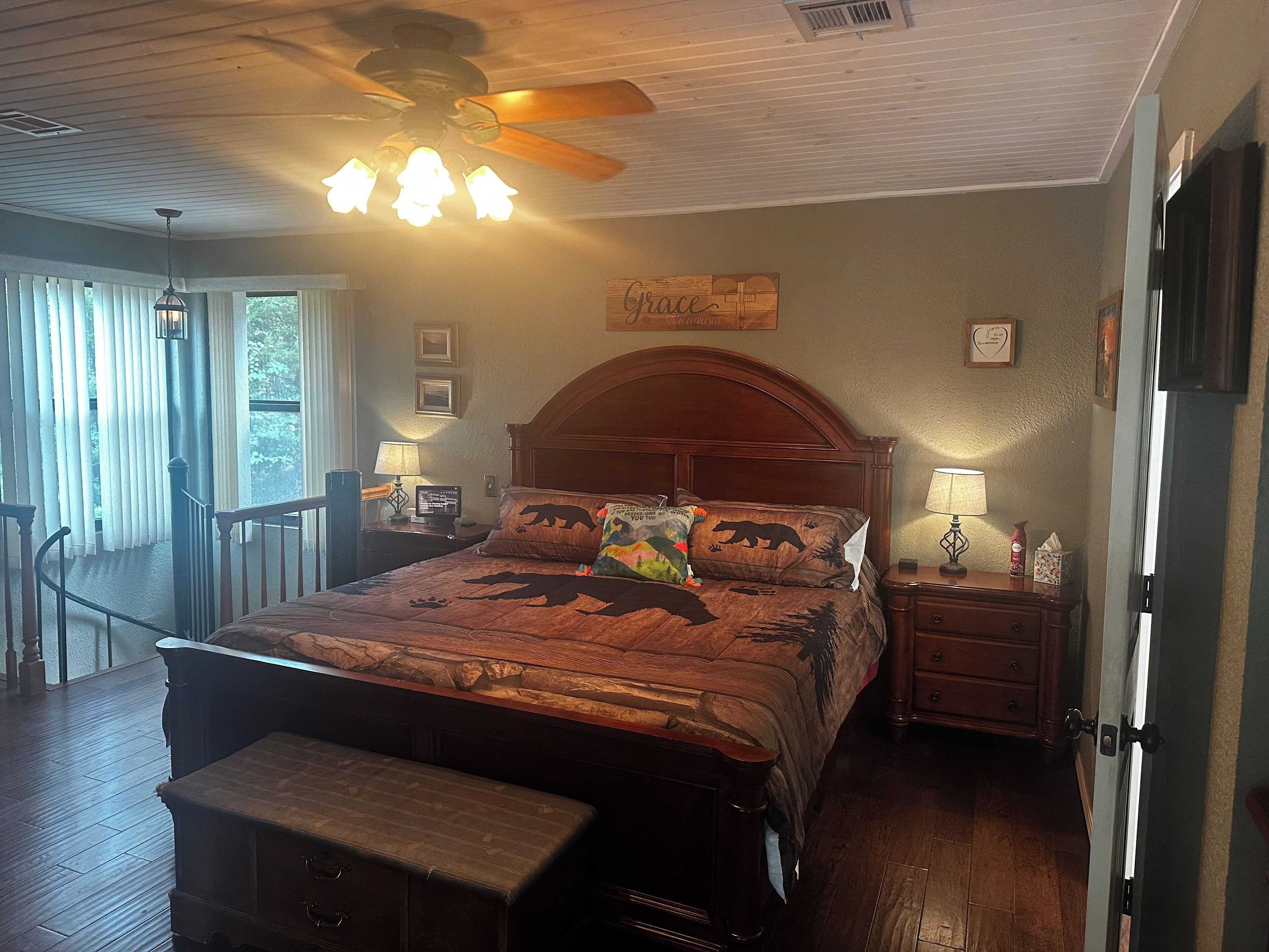 Quarto com cama de madeira, um banco, ventilador de teto e vista para o exterior.