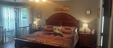 Quarto com cama de madeira, um banco, ventilador de teto e vista para o exterior.