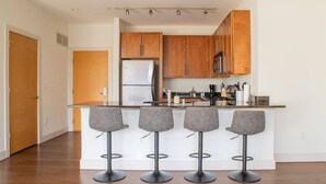 A modern kitchen with wooden cabinets, a stainless steel refrigerator, a microwave, and four bar stools. - Upscale Apartment Near Lake Michigan · Sleeps 6-7 (Milwaukee)