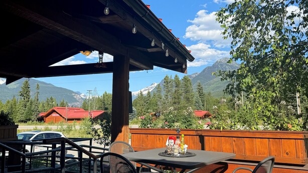 An outdoor patio with a table and chairs, a wooden fence, and a view of mountains and trees. - Blue River Motel (Blue River)