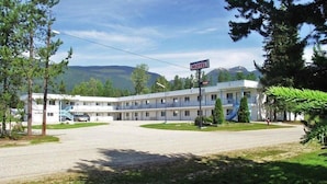 A motel with a two-story building, a covered parking area, and a mountainous backdrop. - Blue River Motel (Blue River)