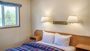 A neatly made bed with a plaid blanket, two bedside lamps, and a nightstand with a lamp. - Blue River Motel (Blue River)
