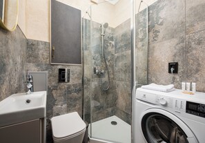 Un baño moderno con ducha acristalada, lavadora integrada y lavamanos.