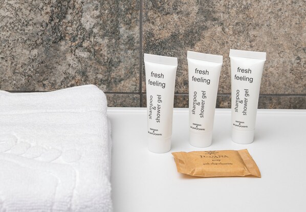 Three white tubes of shampoo and shower gel on a white surface with a granite countertop in the background.