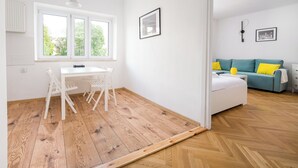 Une pièce avec un plancher en bois, des meubles blancs, une fenêtre donnant sur un beau paysage et un canapé turquoise agrémenté de coussins jaunes.