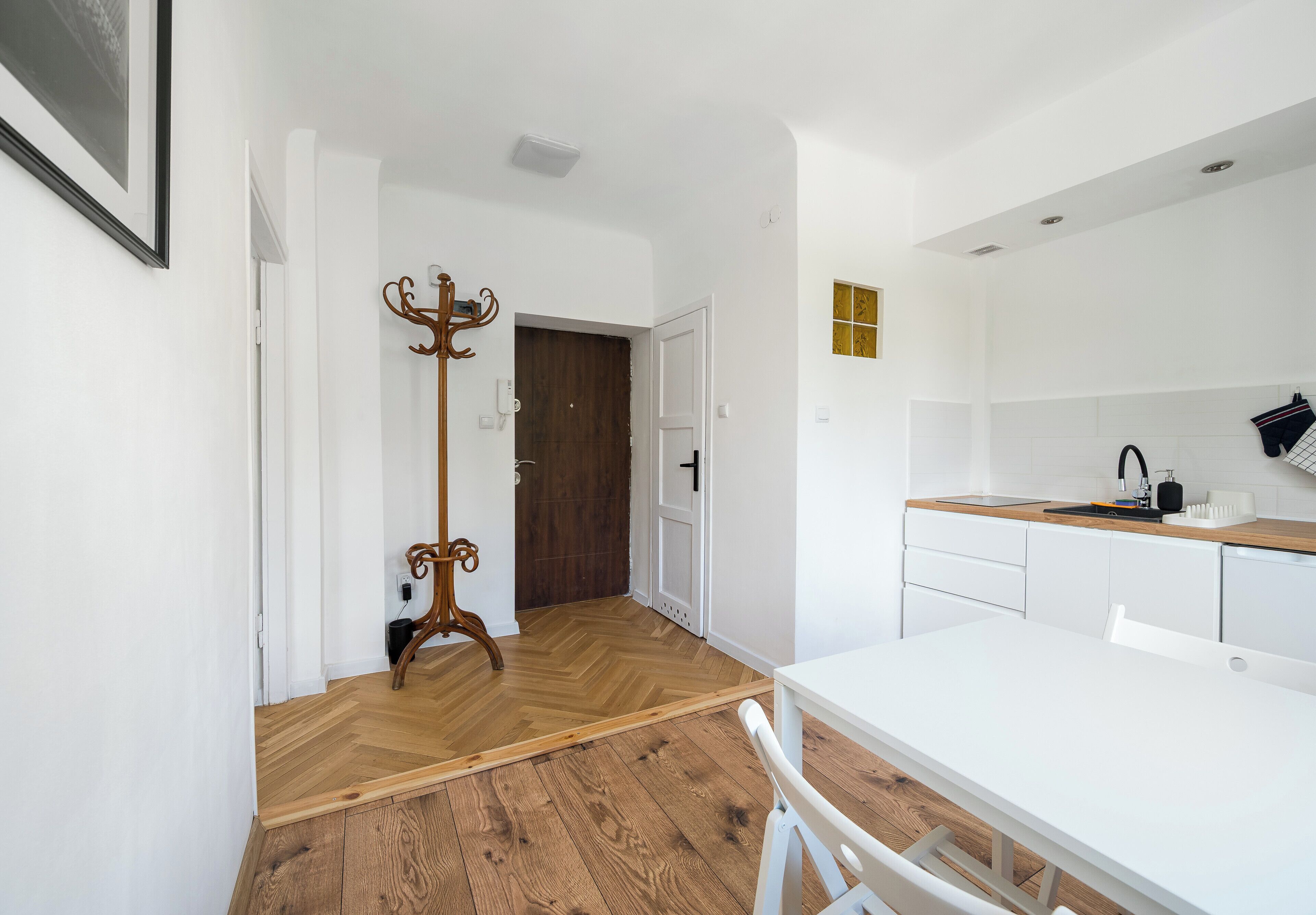 A modern kitchen with white cabinetry, a wooden herringbone floor, and a white dining table.