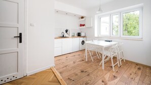 Une cuisine moderne avec des meubles blancs, un plancher en bois et un coin repas avec des chaises blanches.
