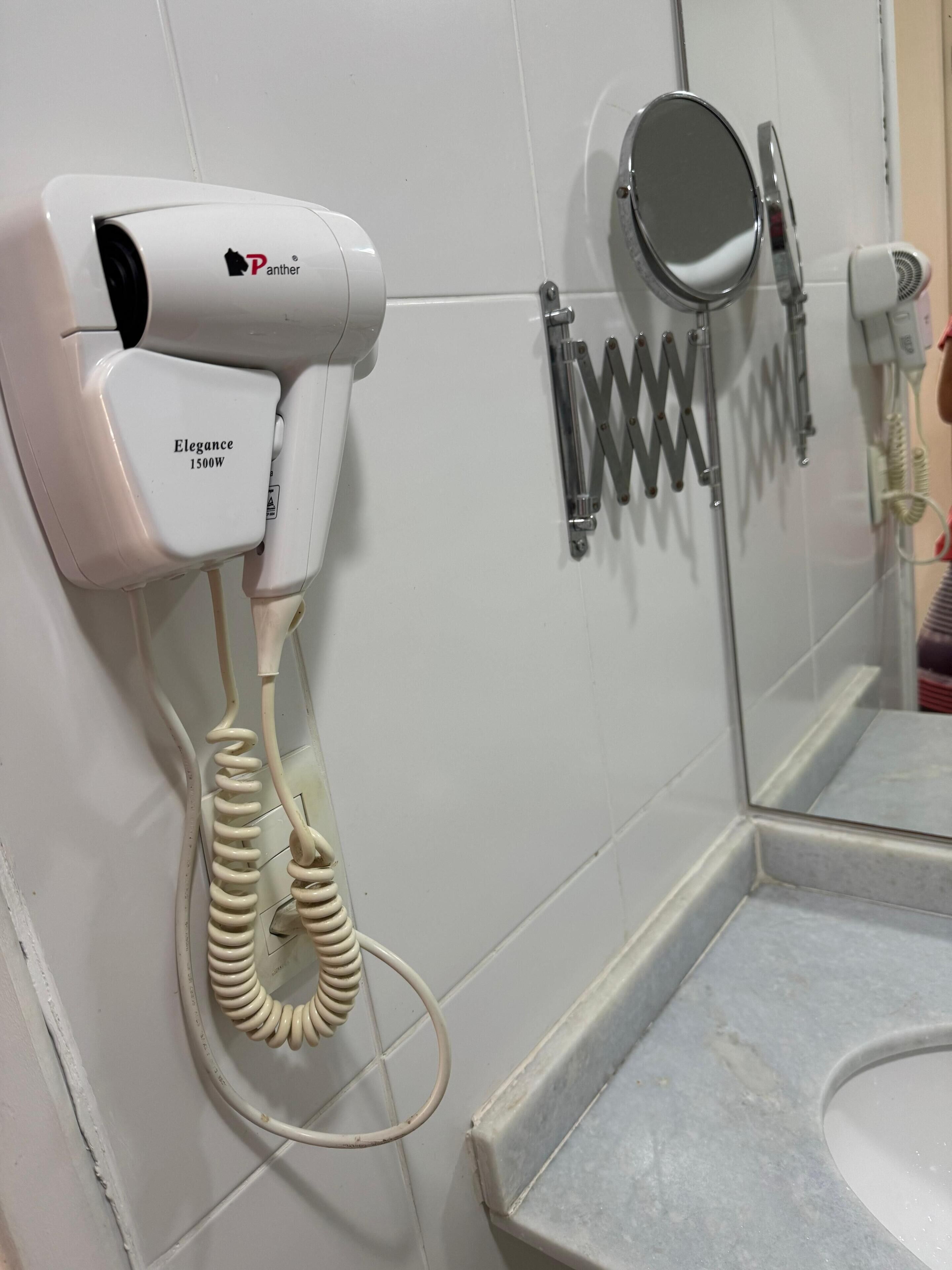 Une salle de bain équipée d’un sèche-cheveux fixé au mur, d’un miroir et d’un porte-serviettes.