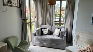 Un dormitorio moderno con una cama grande, un sofá gris, un sillón verde y una ventana con cortinas.