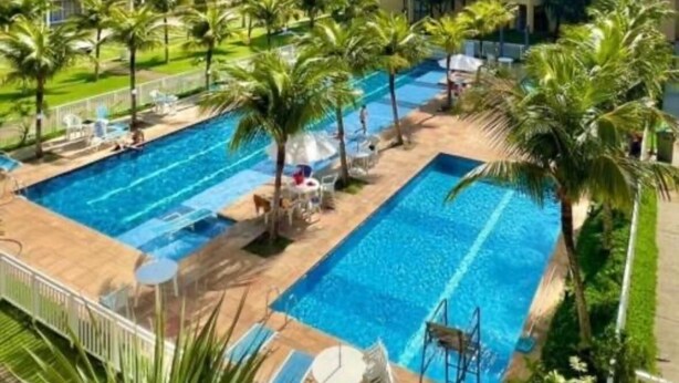 Piscina con varias pistas, rodeada de palmeras y sillas de descanso, con edificios al fondo.