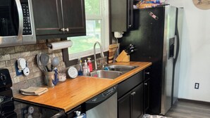 A modern kitchen with dark cabinets, stainless steel appliances, a wooden countertop, and a patterned rug. - The Lakeview Cabin (Clarkson)