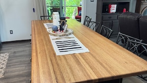 A wooden kitchen island with a central island bar, a dining table with chairs, a kitchen cabinet, and a view of greenery outside. - The Lakeview Cabin (Clarkson)
