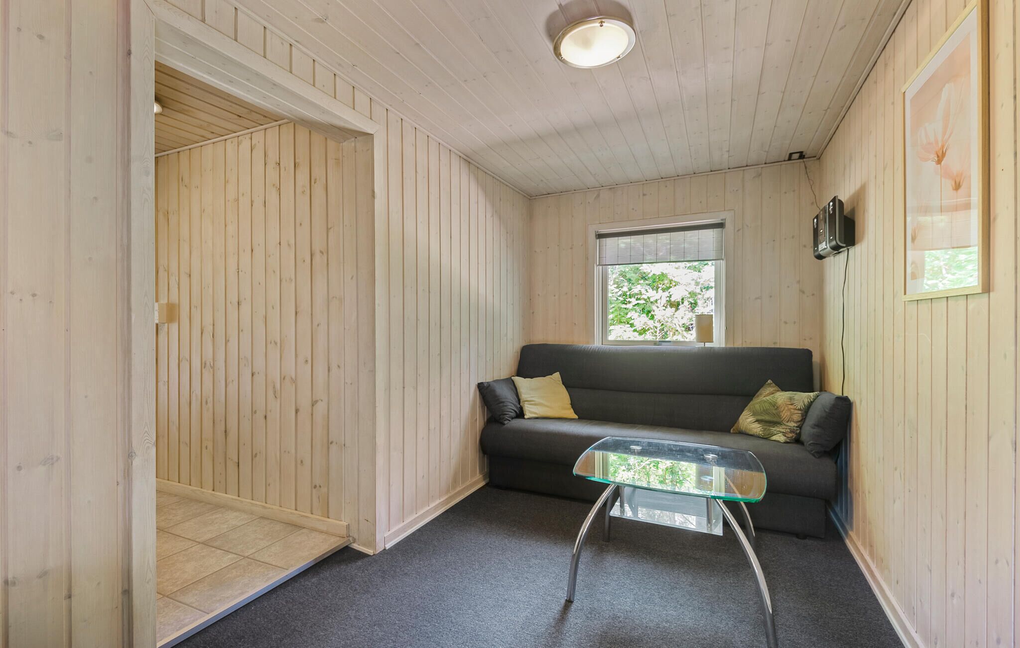 Una habitación acogedora con un sofá gris oscuro, una mesa de centro de cristal y una puerta de madera que da a otro espacio.