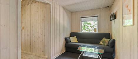 Una habitación acogedora con un sofá gris oscuro, una mesa de centro de cristal y una puerta de madera que da a otro espacio.