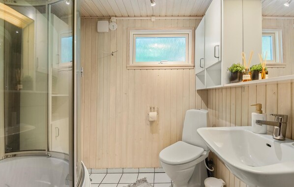 A bathroom with a glass shower enclosure, a toilet, a sink, and a window above the toilet.