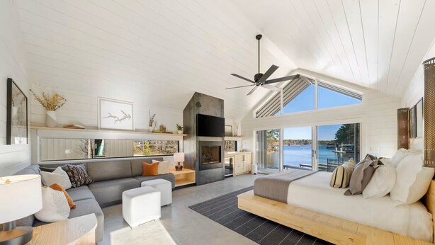 A modern living room with a large sofa, a dining area, and a kitchen. There is a large window providing a view of the outdoors. - Charming 2-bedroom, lakeside cabin at Lake Cypress Springs in Mt. Vernon, TX (Mount Vernon)