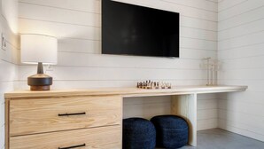 A modern room with a wooden desk, a flat-screen TV, a lamp, and two blue ottomans. - Charming 2-bedroom, lakeside cabin at Lake Cypress Springs in Mt. Vernon, TX (Mount Vernon)