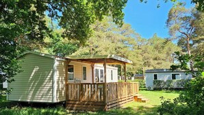 Ein kleines, eingeschossiges Mobilheim mit einer Holzterrasse und einer überdachten Veranda.