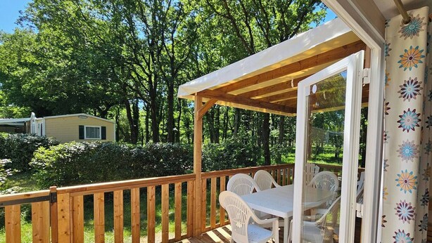 Eine Holzterrasse mit Tisch und Stühlen, umgeben von einem Holzgeländer, mit Blick auf eine üppige grüne Landschaft.