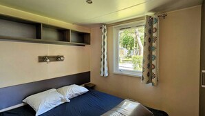 Ein Hotelzimmer mit Bett, einem kleinen Nachttisch, einem Fenster mit blumigen Vorhängen und einem Kopfteil mit integrierten Regalen.