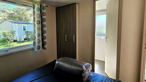 Eine kleine, einfache Unterkunft mit einem Bett, einem Kleiderschrank und einem fenster mit Vorhängen.