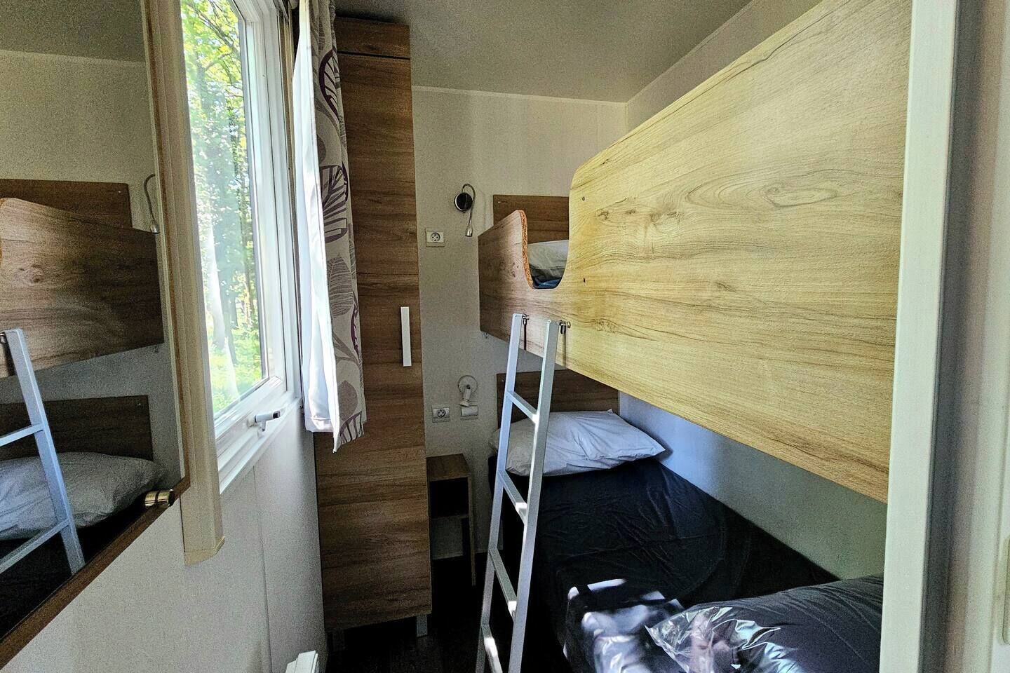 Een kleine, goed verlichte kamer met stapelbedden, een raam met gordijnen en een houten wand.