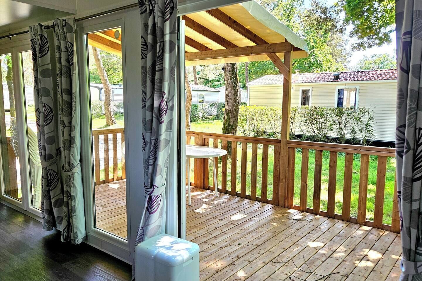 Een overdekt terras met houten balustrade, een tafel en uitzicht op een woonwijk met huizen en bomen.