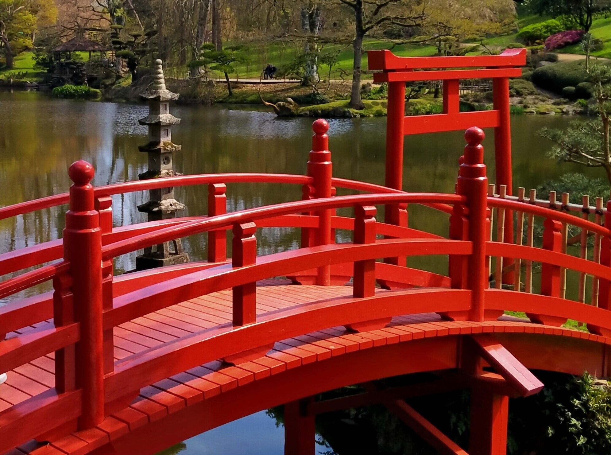 Eine rote Brücke über einen Teich, im Hintergrund ein Pagode.