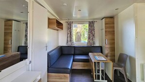 Interior compacto de una caravana con un sofá, una mesita y una ventana con cortinas.