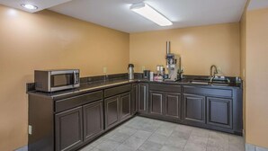 A compact kitchen with dark cabinets, a microwave, a coffee maker, and a sink. - HomeTown Inn & Suites (Macon)