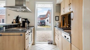 Una cocina moderna con armarios de madera, una campana extractora de acero inoxidable y un amplio ventanal con vista a una zona residencial.