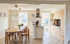 A modern kitchen with a central island, wooden cabinets, and a dining area with a table and chairs. - Gorgeous home in Rømø with house a panoramic view (Rømø)