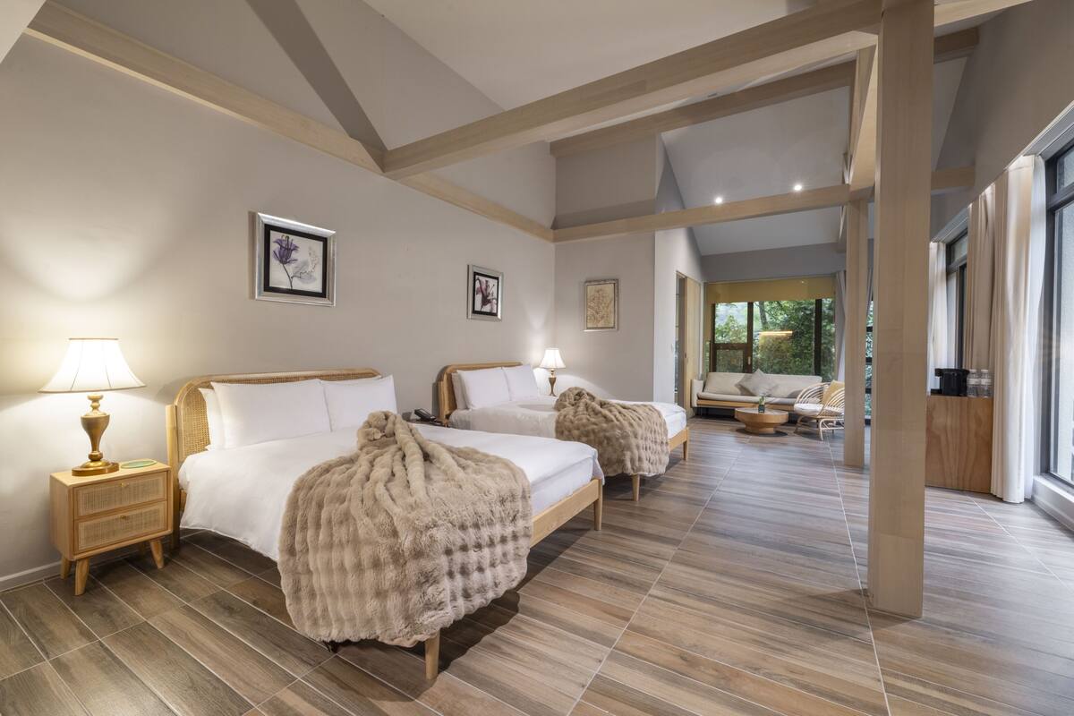 Habitación de hotel con dos camas, pisos de madera y vista al exterior.