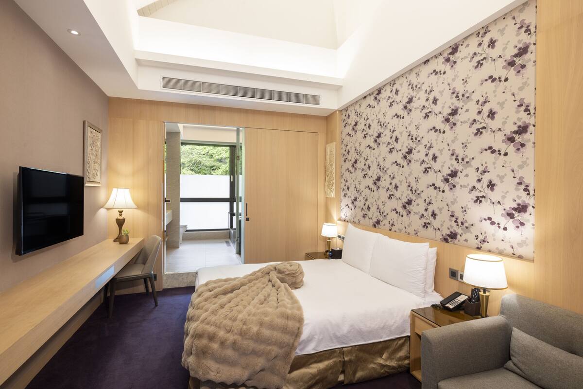 Una habitación de hotel con cama, televisión, escritorio con lámpara, silla y sofá.