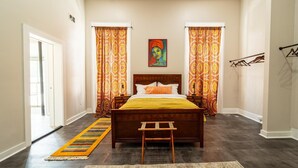 Un dormitorio con cama de madera, cortinas estampadas, un cuadro en la pared y un pasillo con alfombra.