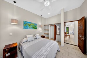 Une chambre à coucher comprenant un lit, des tables de chevet, un ventilateur de plafond, un tableau et une armoire.