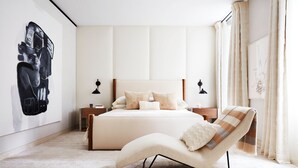 A modern bedroom with a large bed, a chair, and a wall art piece.