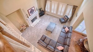A spacious living room with a fireplace, leather sofa, and large windows.