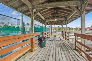 Une terrasse en bois couverte, dotée de bancs et de tables de pique-nique, et entourée d’une clôture en treillis métallique.