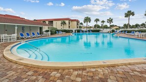 Una piscina con acqua azzurra, circondata da sdraio e un edificio con tetto rosso.